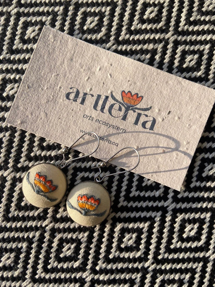 These hand-embroidered earrings are a creation of Dao Donjerm, an artist based in Vancouver, BC. The earrings feature the artterra flower design, making them a unique and stylish addition to any outfit. Shop for one-of-a-kind jewelry pieces like these at the artterra art gallery